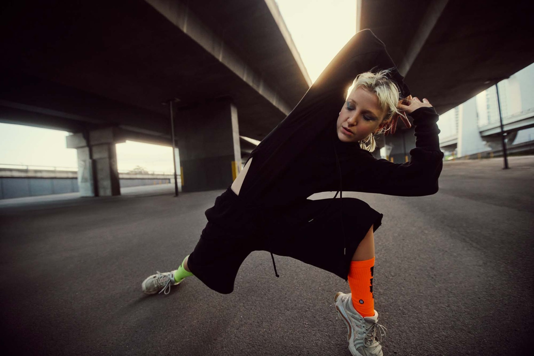 hip-hop-dancer-stretches-toward-camera-under-overpass-roads