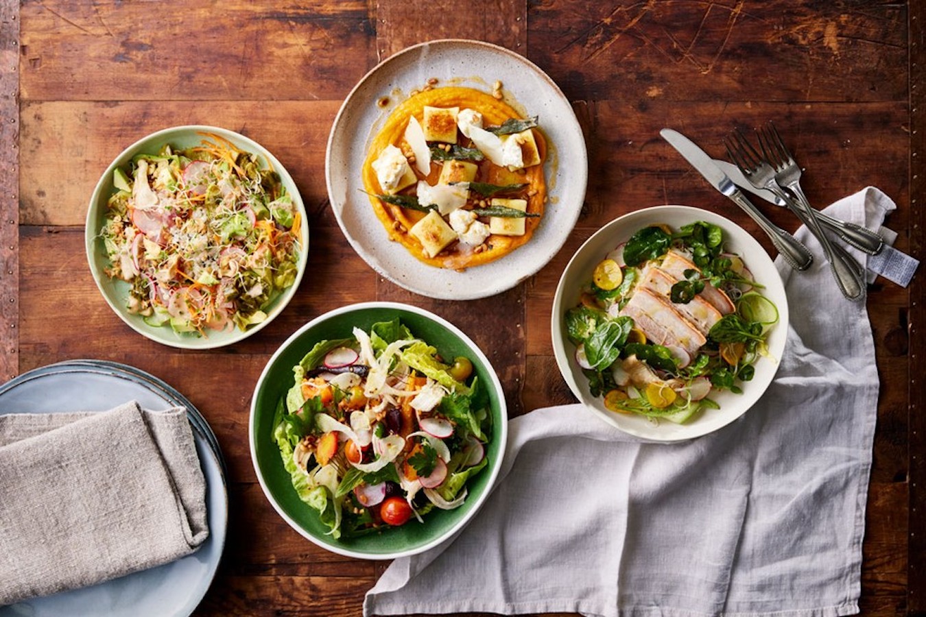 An overhead shot of four dishes: gnocchi, chicken salad, pork salad and veggie salad