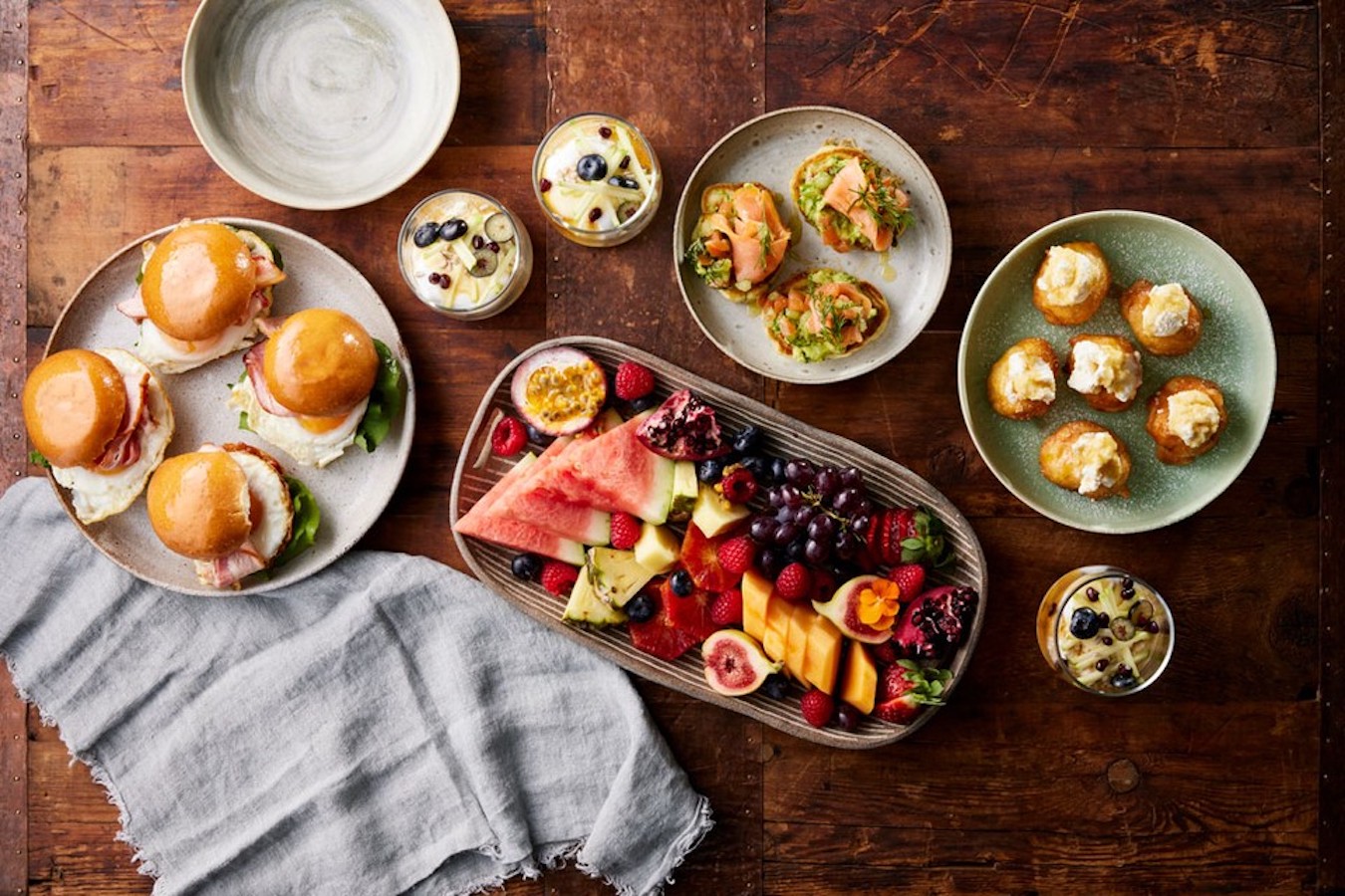 Overhead shot of Sokraa's Kitchen spread including burgers, fruit platter, parfait, salmon and avocado.