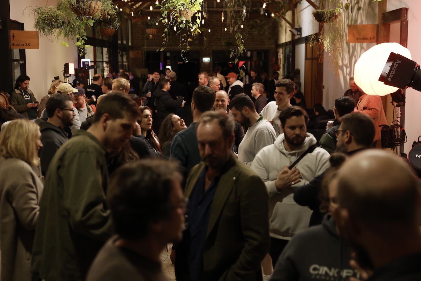 A crowd of people gathered in SUNSTUDIOS Atrium, with potted plants hanging from the ceiling