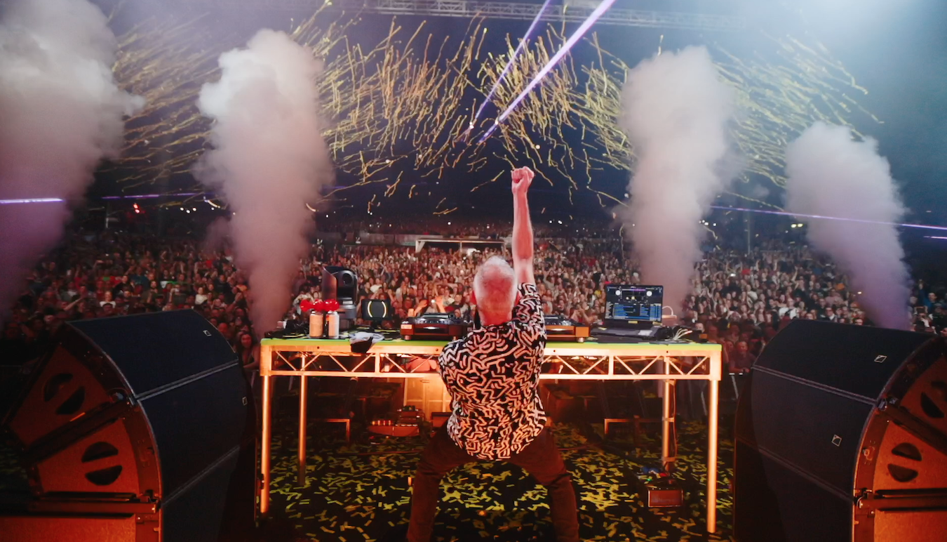 Fatboy Slim performing on stage at his concert, image taken from behind showing the crowd