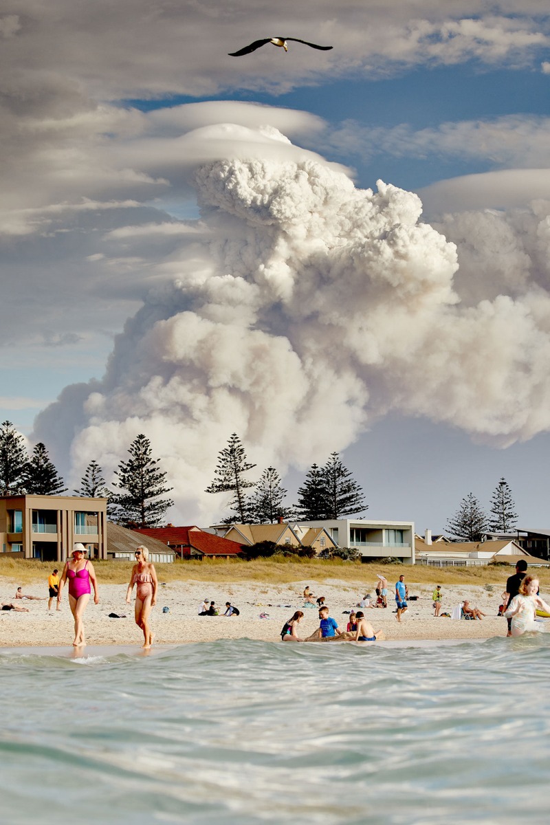 colourful-beach-scene-withhumans-swimming-in-the-foreground-seemingly-oblivious-to-a-mushroom-cloud-of-fire-n-the-background