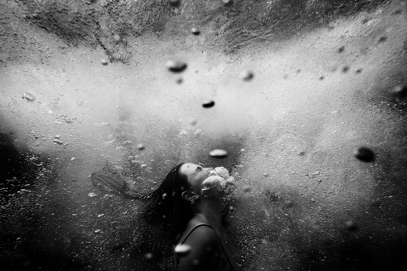 black-and-white-image-of-girls-face-underwater-beginning-to-exhale-large-bubbles-before-breaking-the-surface-to-breathe-again