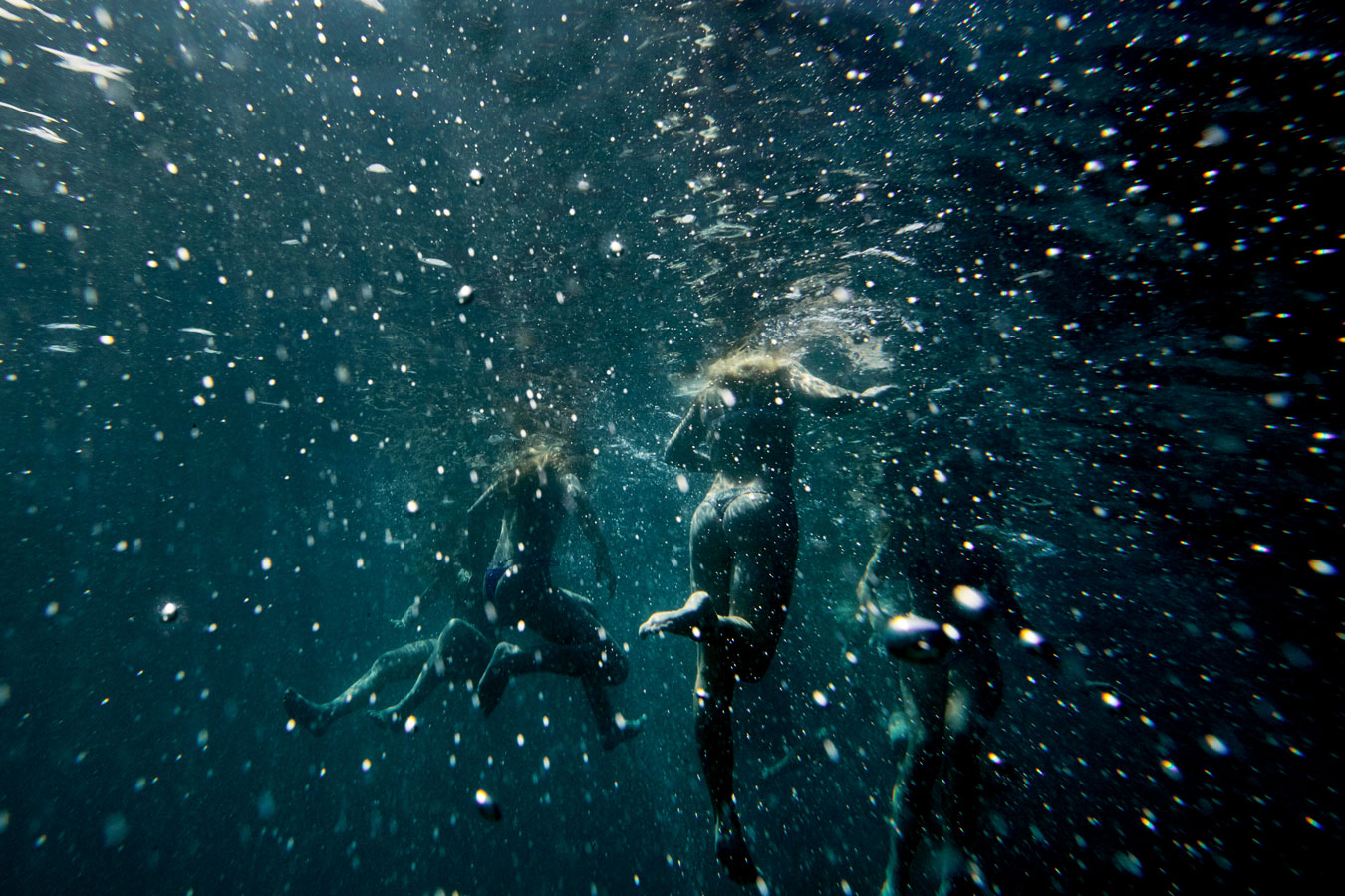 several-people-kicking-to-stay-boyant-underwater-you-can-see-legs-under-feet-in-dark-turquoise-bubble-space