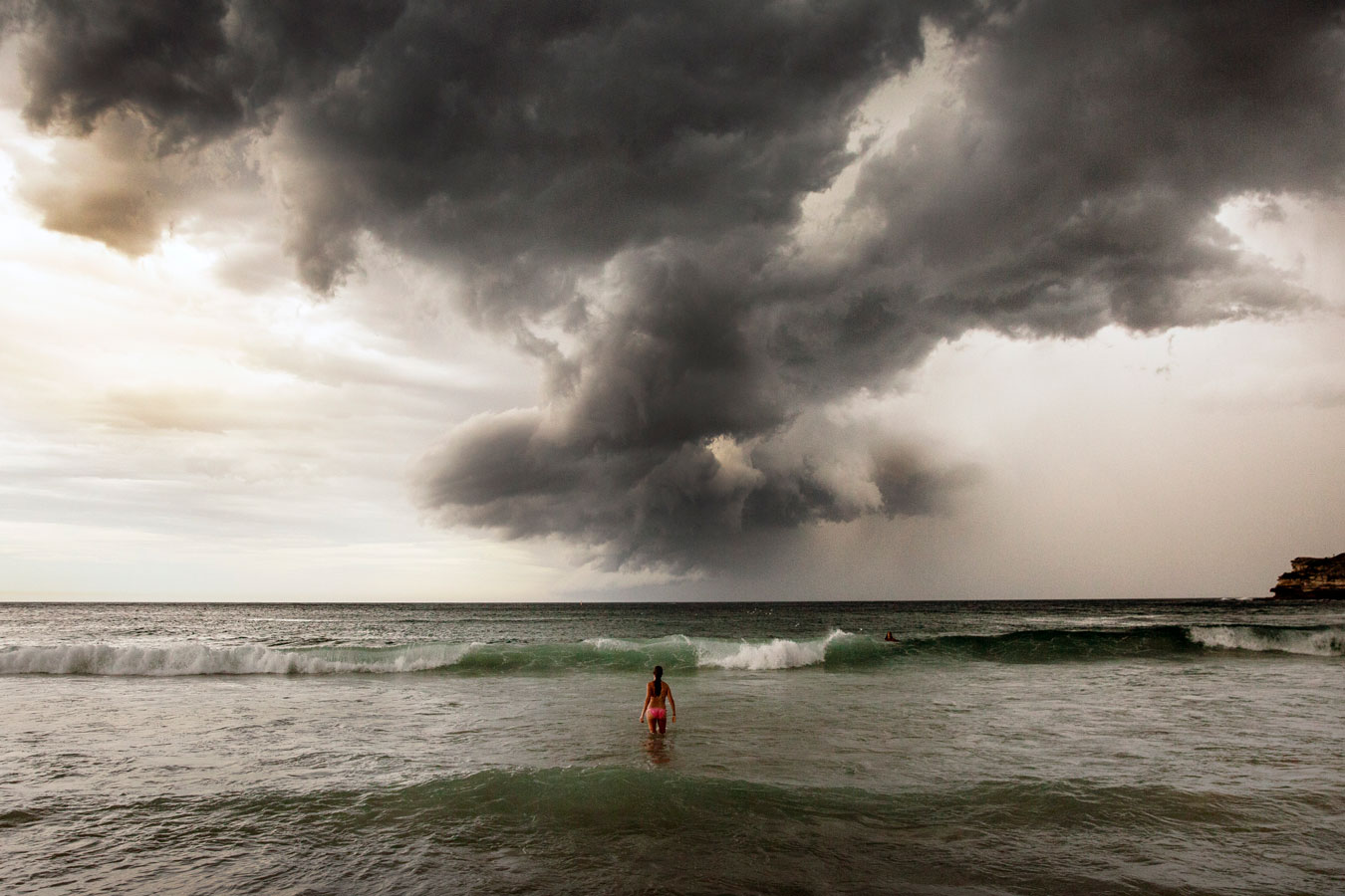 woman-with-back-turned-wading-into-the-ocean-as-a-tornado-like-storn-dwarves -her-in-the-distance