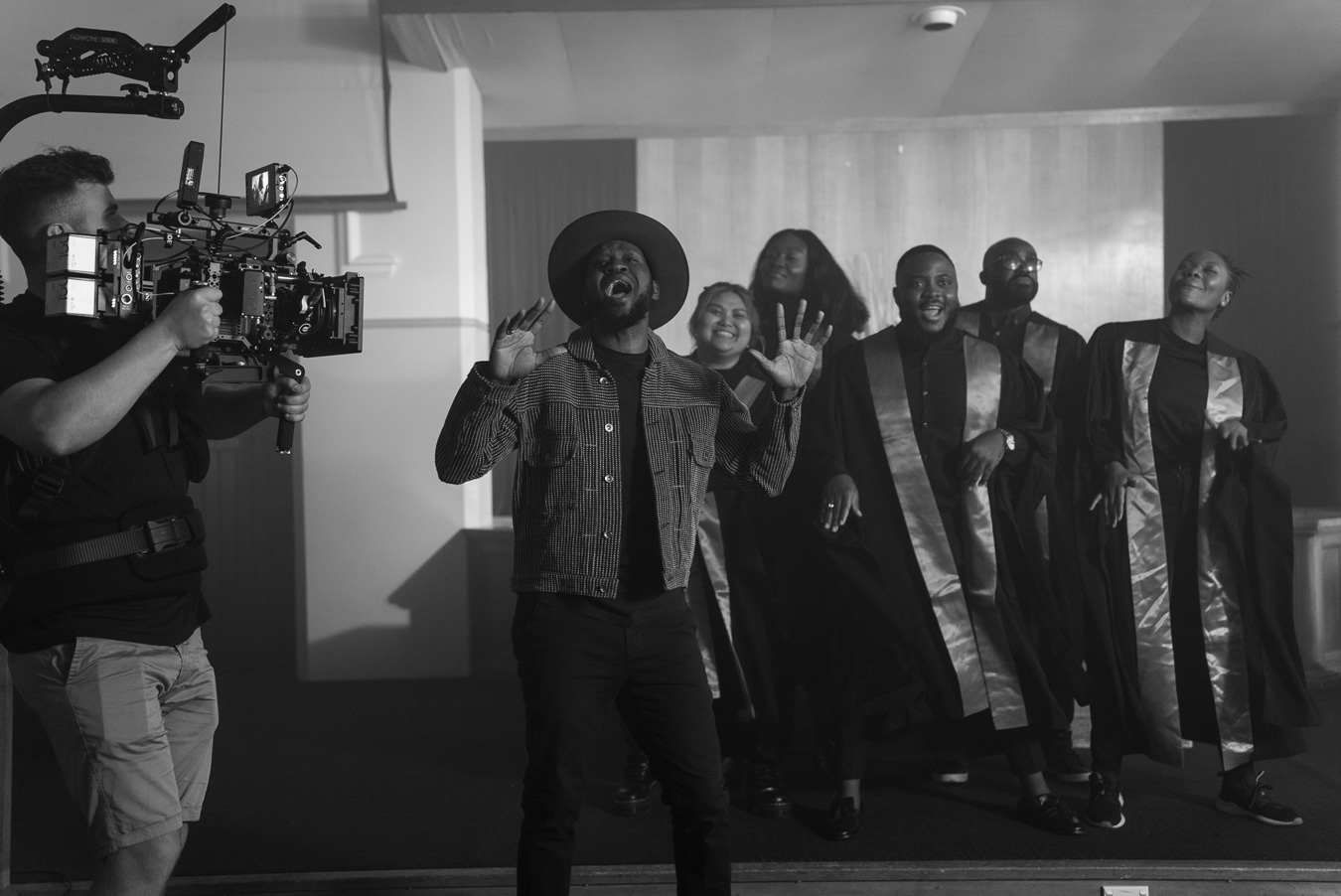 black-and-white-behind-the-scenes-image-of-man-holding-camera-rig-while-singer-and-church-choir-perform