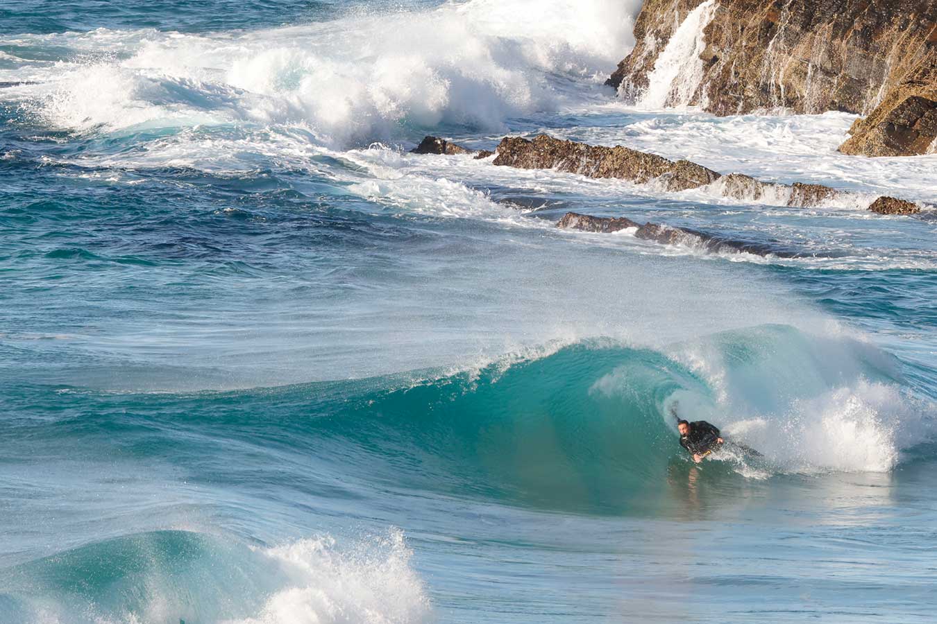 surfer-mid-aqua-wave-curl-with-rocks-in-background