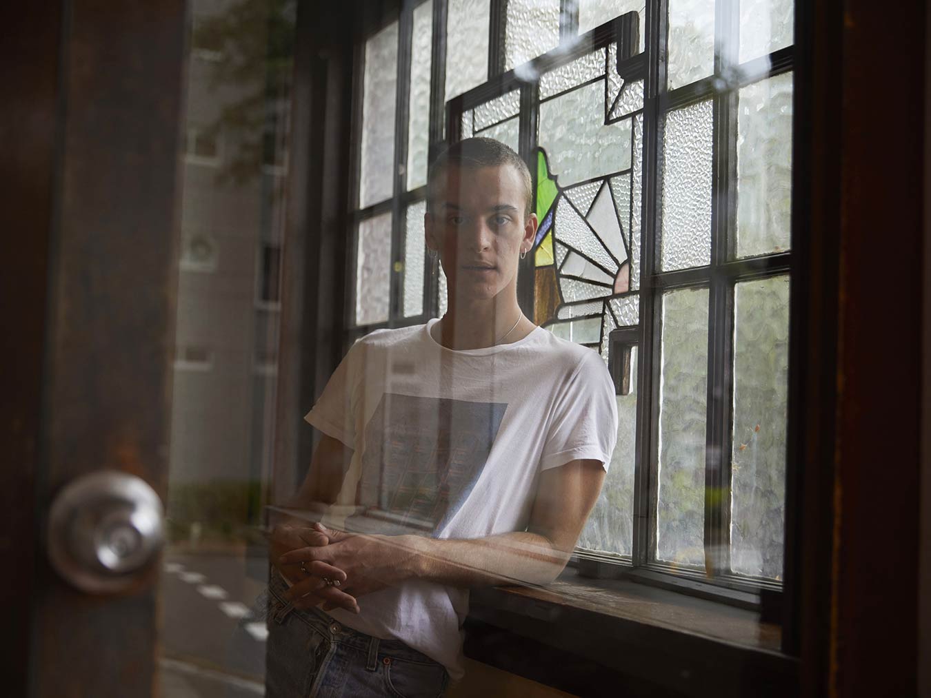 portrait-of-aris-person-standing-near-stainglass-windows-with-glass-reflections