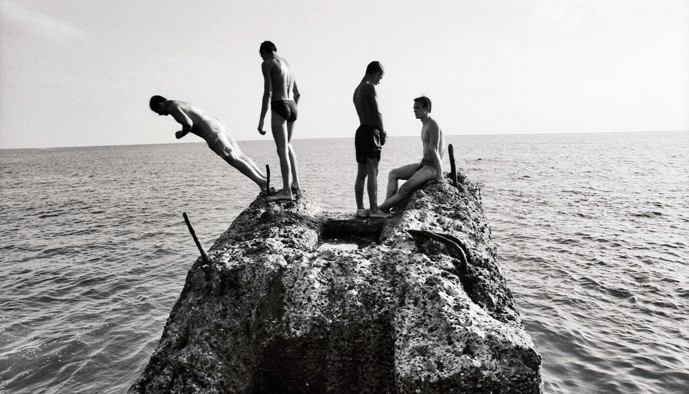 four-young-teen-boys-in-different-stages-of-jumping-off-a-rock