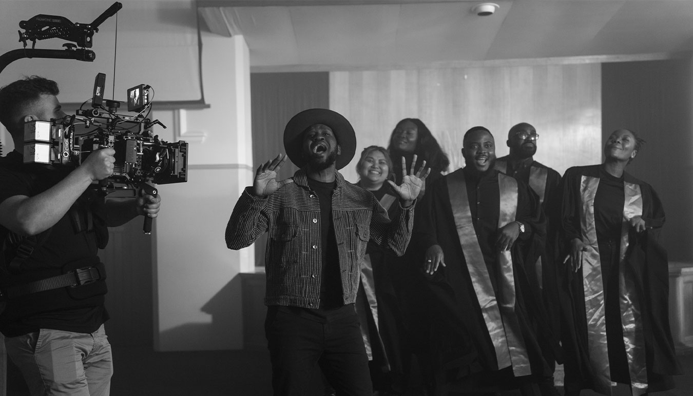 black-and-white-behind-the-scenes-image-of-man-holding-camera-rig-while-singer-and-church-choir-perform