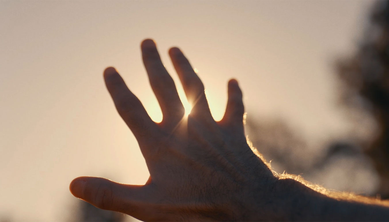 a-hand-reaches-to-partially-obstruct-the-sun-in-golden-afternoon-light