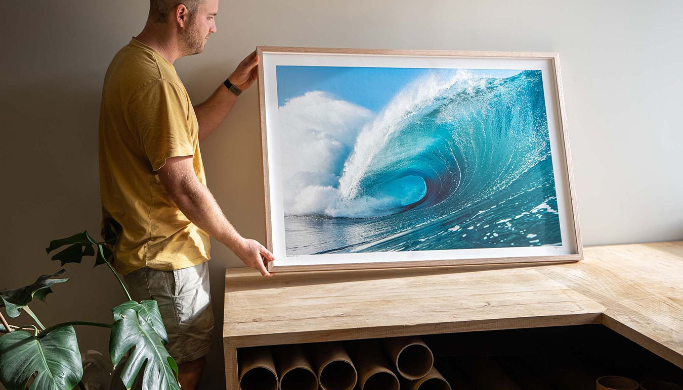 man-in-tshirt-holding-framed-photograph-of-a-wave