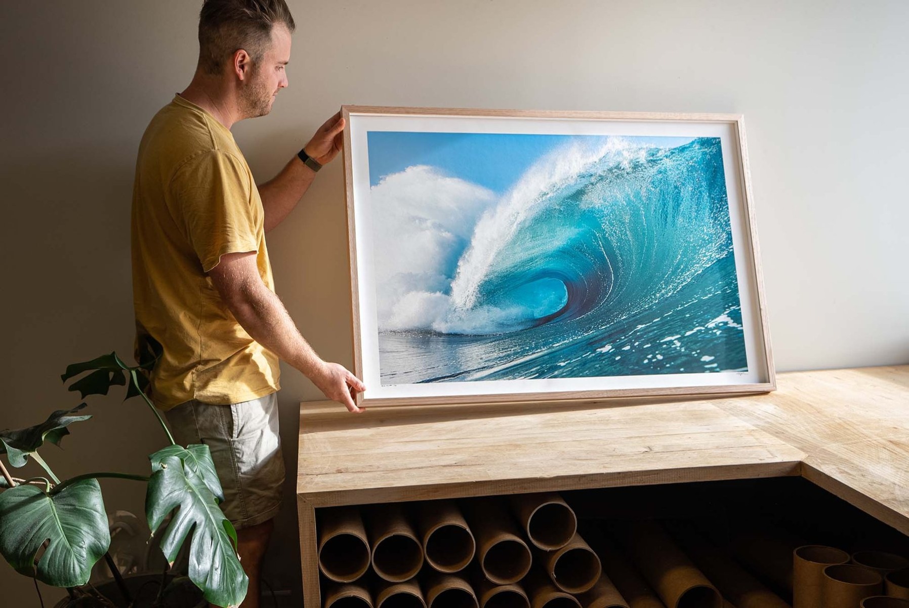 man-in-shirt-holds-framed-ocean-photogrpah-in-natural-window-light